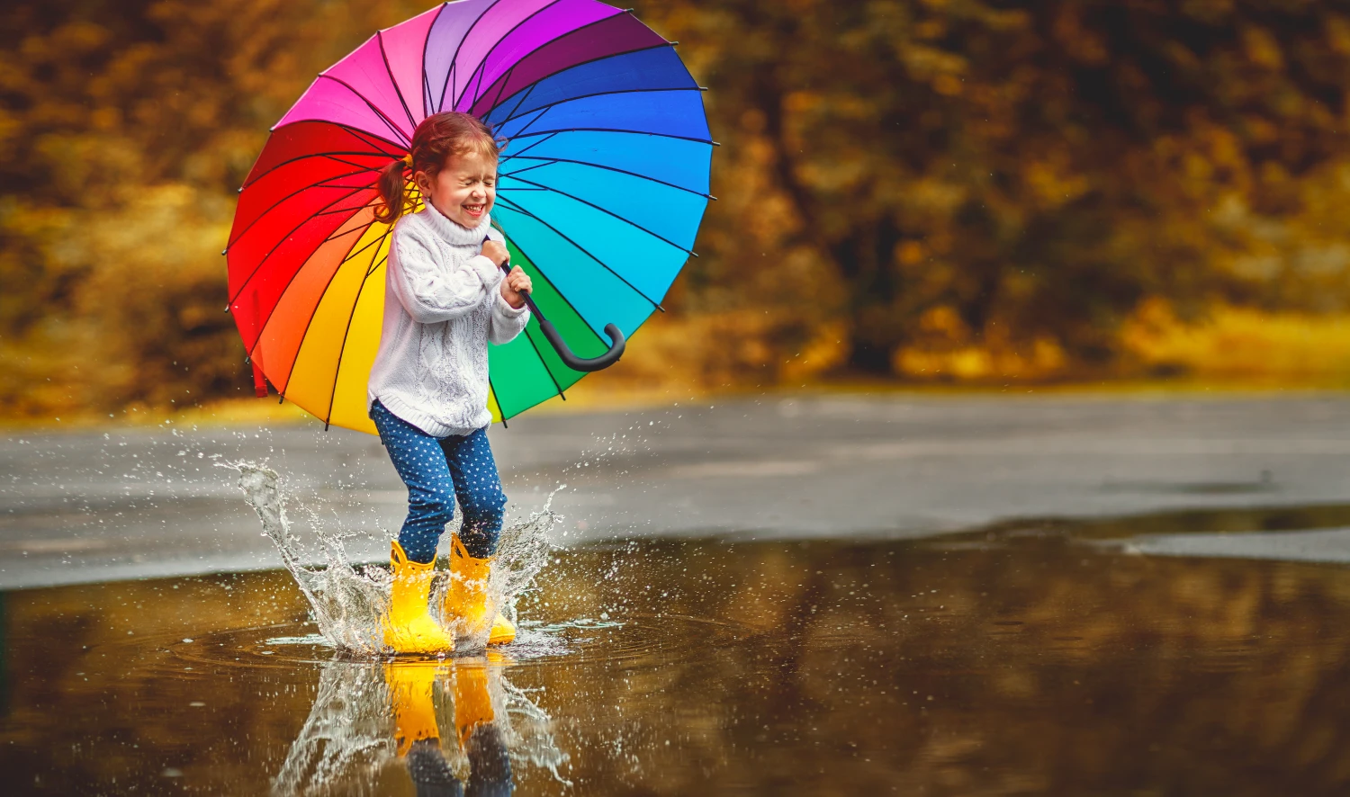 Ein kleines Mädchen spielt im Regen und hält einen Regenschirm in der Hand von Kindertagespflege
